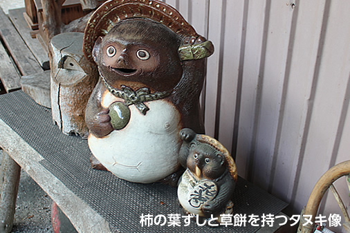 柿の葉ずしと草餅を持つタヌキ像