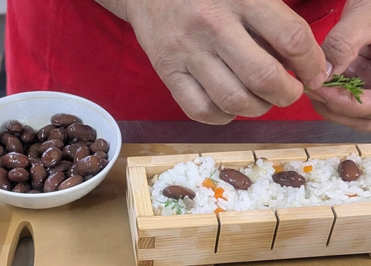 詰めた酢飯の上に均一に金時豆を並べ、ニンジン葉を飾り付ける